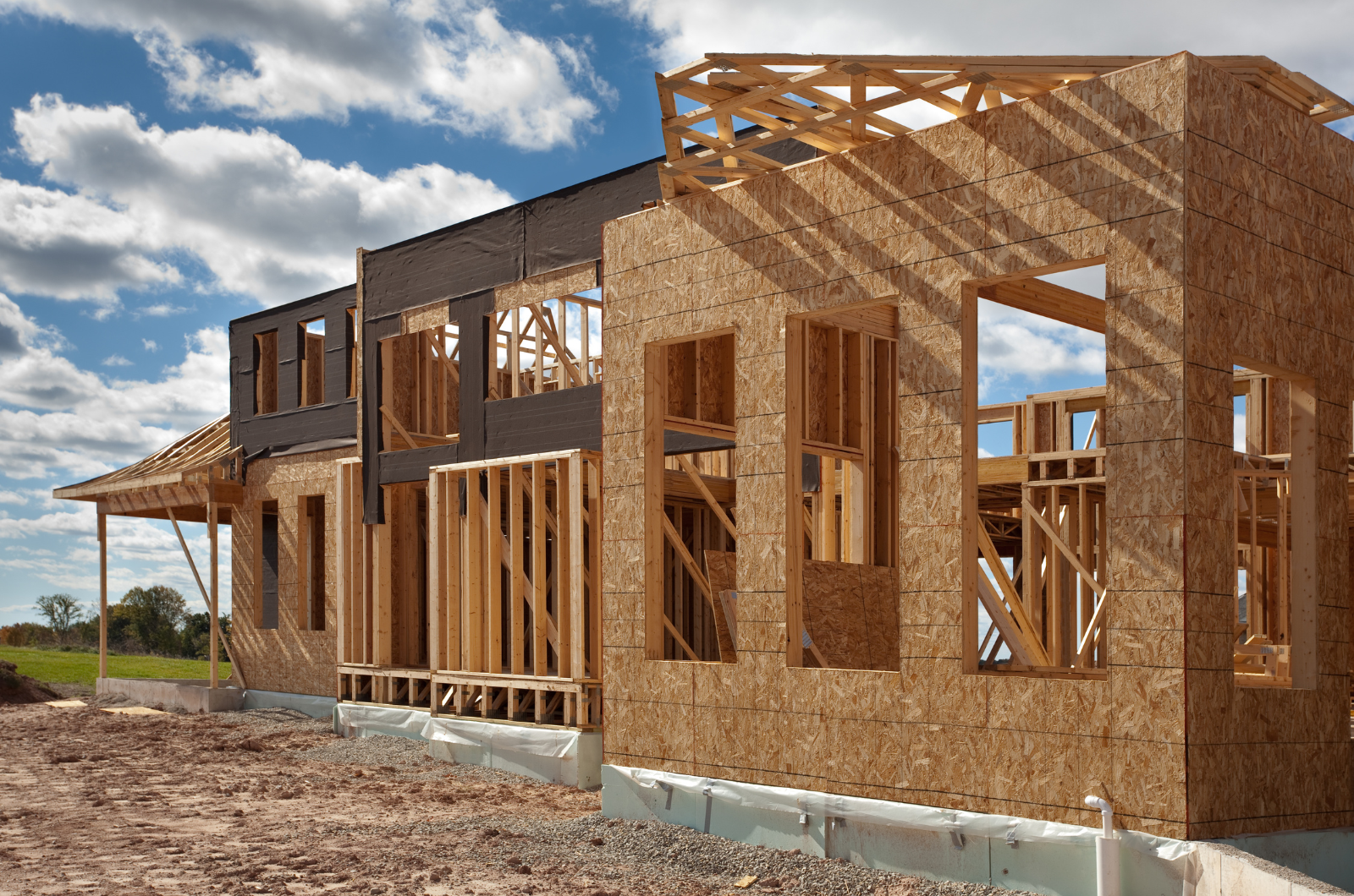 Wood-framed house under construction on an open site with blue sky