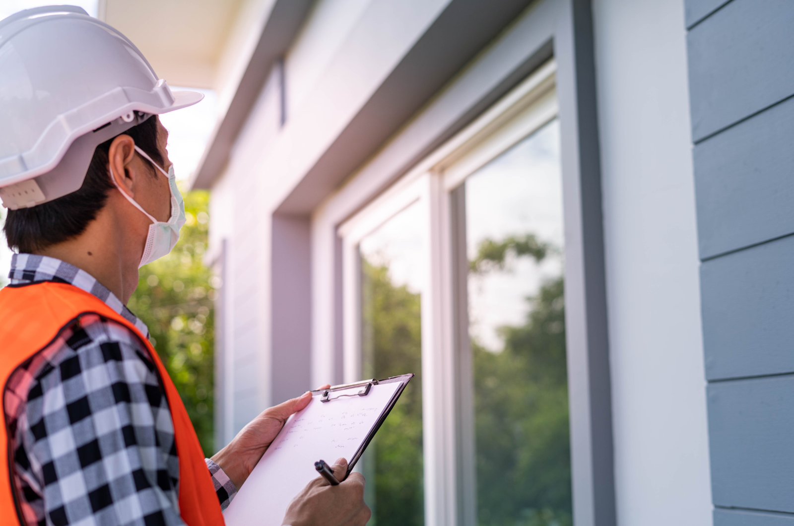 Construction worker inspecting house exterior with checklist